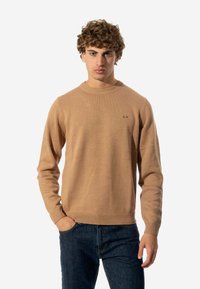 Maglione beige con scollo a girocollo, realizzato in materiale a maglia. Presenta un piccolo logo sul petto e polsini e orlo a costine.