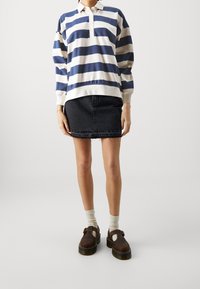 Pruhovaný pulovr v námořnické modré a krémové barvě s límečkem a třemi knoflíky, kombinovaný s černou džínovou sukní. Hnědé boty s přezkou.