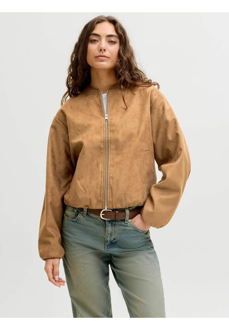 Braune Wildlederbomberjacke mit einem Reißverschluss und einem runden Kragen, kombiniert mit hellblauen Jeans und einem braunen Gürtel. Weiche Textur und lässige Passform.