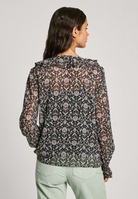 Blusa nera trasparente con motivo floreale in blu, rosa e verde. Presenta un colletto arricciato e maniche lunghe con polsini arricciati.