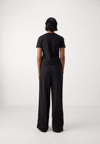 Camiseta de algodón negra de manga corta, con un torso ajustado, combinada con pantalones negros de pierna ancha que presentan un sutil detalle de bolsillo trasero.