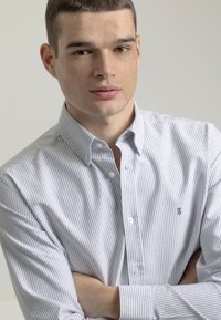 Camisa de botones a rayas en algodón blanco y gris claro con cuello, que presenta un patrón de rayas estrechas y un pequeño logo bordado en el pecho.