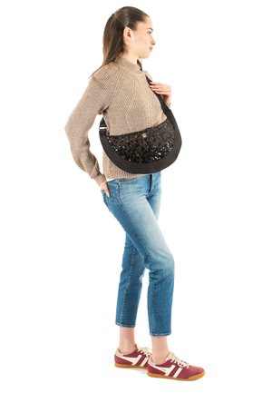 Borsa nera con paillettes lucenti sulla parte anteriore, forma curva, tracolla regolabile, indossata a tracolla. Modella con maglione beige e jeans blu.