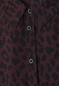 Chemise violet foncé boutonnée avec motif léopard noir et col pointu.