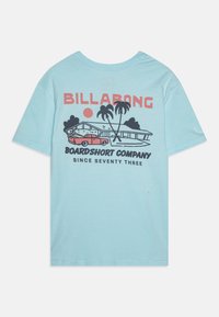 T-shirt in cotone verde menta con una grafica di un'auto, palme e una casa, con il testo "BILLABONG BOARDSHORT COMPANY".