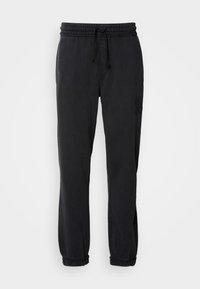 Black sweatpants with an elastic waistband and drawstring. Gathered hems and a subtle embroidered logo on the left leg. Soft fabric texture.