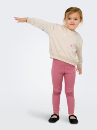 Lichtbeige sweatshirt met kleurrijke bloemenstickers, gecombineerd met geribbelde roze legging. Zwarte platte schoenen maken de outfit compleet.