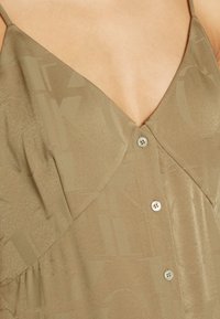 Khaki šaty s výstřihem do V, tenkými ramínky a zapínáním na knoflík. Hladká textura s jemným vzorem loga na látce.