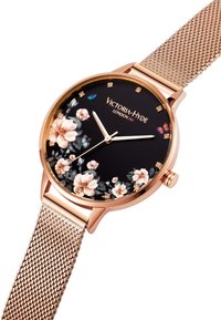Damenuhr mit einem roségoldenen Edelstahlnetzarmband und einem schwarzen Blütendiagramm. Sie ist mit goldenen Akzenten und Kristallen verziert und zeigt den Markennamen Victoria-Hyde London.