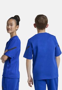 Camiseta deportiva azul real de manga corta, con cuello redondo y acentos de rayas negras en los hombros. Hecha de un tejido suave y transpirable.