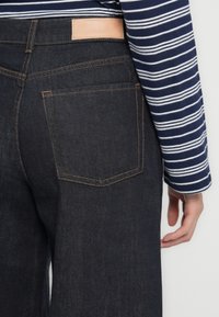 Mørkeblå denimjeans med rette ben, kontrasterende oransje sømmer og et brunt lærmerke i livet.