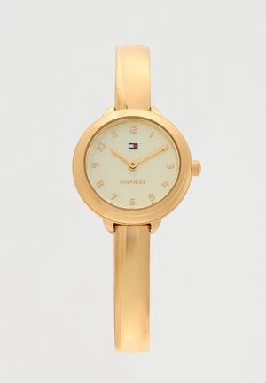 Orologio da polso Tommy Hilfiger color oro con quadrante minimalista che segna le 10:10, cinturino stretto e logo del marchio sotto le 12.