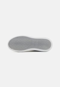 Semelle de chaussure avec une surface grise texturée présentant un motif circulaire, entourée d'une bordure en caoutchouc blanc, de forme légèrement courbée.