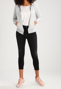 Sudadera con cremallera color gris claro con el logo "GAP", camiseta blanca, jeans negros cortados, y zapatillas color rosa claro con suelas blancas.