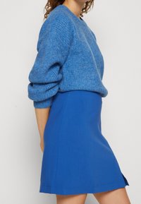 Niebieski sweter z dzianiny z zawiniętymi rękawami, w połączeniu z niebieską dopasowaną spódnicą w kształcie litery A. Tkaniny mają gładką fakturę i jednolity kolor.