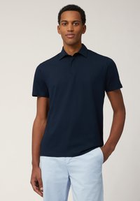 Marineblaue Poloshirt mit klassischem Kragen, kurzen Ärmeln und dezentem Logo auf der Brust. Glatter Baumwollstoff mit taillierter Passform.