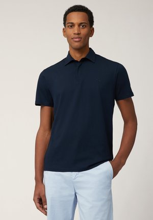 Polo shirt bleu marine avec un col classique, des manches courtes et un logo discret sur la poitrine. Tissu en coton lisse avec une coupe ajustée.