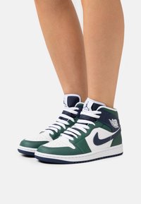 Höga sneakers med en övre del av grön och vit läder, marinblå accenter, perforerad tå och vita snörning. Logotyp på vristen.