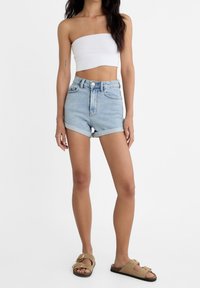 Lichtblauwe denim shorts met een hoge taille en een opgerolde zoom, gecombineerd met een witte strapless top en tan sandalen met gespen.
