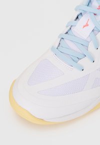 Bottine de sport blanche avec des lacets bleu clair, dotée d'un dessus texturé et d'une semelle jaune pâle. Panneaux en maille notables pour une meilleure respirabilité.