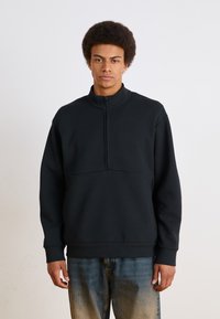 Sudadera negra con cremallera cuartofull, que presenta una textura suave y una sección de tela contrastante por encima de la cintura.