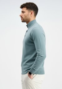 Šviesiai mėlynas ilgomis rankovėmis polo megztinis su aukštu apykakliu ir trimis sagomis, turintis tekstūruotą raštą bei austo audinio rankogalius ir apačią.