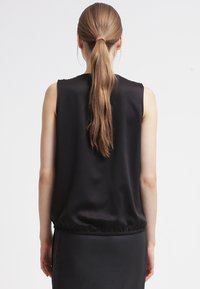 Mustaton hihaton paita rentoa istuvuutta, joustava helma ja sileä satiinimainen tekstuuri. Hiukset sidottu ponihännälle, keskittyen takaosaan.