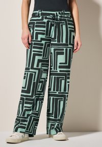 Luźne, jasne miętowe spodnie z czarnym geometrycznym wzorem. Posiadają elastyczny pas i sznurek do regulacji, wykonane z miękkiego, teksturowanego materiału.