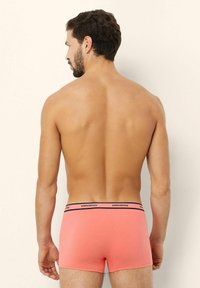 Korallinväriset boxerkalsonger, som är gjorda av mjukt tyg. De har en svart midjeband med "yamamay"-text. Kort, åtsittande design som täcker midjan och övre låren.