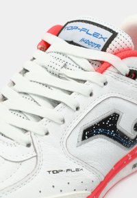 Bela športna obutev iz perforirane usnje, črne in modre poudarke ter rdečim podplatom. Ima izstopajoč logotip in debele ravne vezalke.