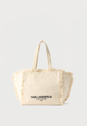 Béžová plátěná taška přes rameno s třásněmi, dvěma uchy a černým logem "Karl Lagerfeld 21 Rue St-Guillaume Paris" uprostřed přední strany.