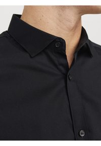 Czarna bawełniana koszula z klasycznym kołnierzykiem, z detalami guzików i gładką teksturą. Zbliżenie ukazuje jakość szwów i tkaniny.