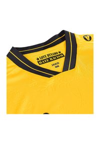 Gele sporttrui met een zwarte V-hals, voorzien van reliëf bloemenpatronen en tekst die "LOVE DINAMO HATE RACISM" in zwart zegt.