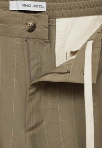 Světle khaki kalhoty s proužkovým vzorem. Mají zipový klín, zapínání na knoflík a látkový pas s nastavitelným stahovac�ím šňůrkou.