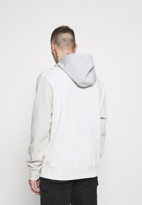 Sudadera con capucha en gris claro con una capucha de un gris más oscuro en contraste. Presenta mangas largas, puños acanalados y un corte relajado.