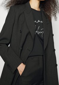 Blazer negro de doble botonadura con rayas verticales, solapas de pico y botones negros. Combinado con una camiseta gráfica negra. Ajuste entallado.