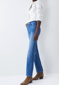 Jeans rectos de mezclilla de color azul claro, con un diseño clásico de cinco bolsillos y una cintura de altura media. Combinados con botas de tobillo de ante marrón.