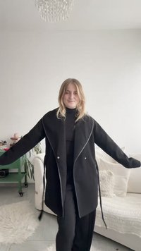 Svart kappa med draperad design, med dragkedjedetaljer och lös passform. Tillverkad av ett texturerat tyg, inkluderar knytband i midjan.