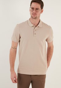 Beige polo tričko vyrobené z texturované látky, s límečkem, tříknoflíkovou légou a krátkými rukávy.