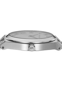 Orologio in metallo argentato con cassa rotonda, quadrante in vetro trasparente, indicatori in numeri romani e logo MK sul lato. Design minimalista.