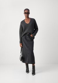 Knitpullover in grafitgrau mit V-Ausschnitt, kombiniert mit einem langen schwarzen Denimrock mit ausgefranstem Saum. Schwarze Knöchelstiefel und eine kleine Tasche.