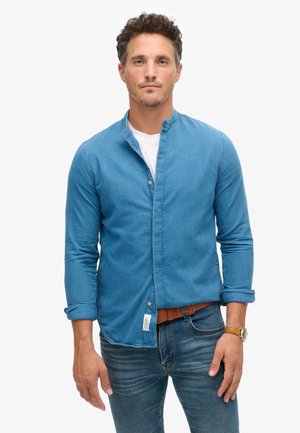 Blauwe denim shirt met een Mandarin-kraag, knoopsluiting en lange mouwen. Draag met lichtblauwe jeans en een leren bruine riem.