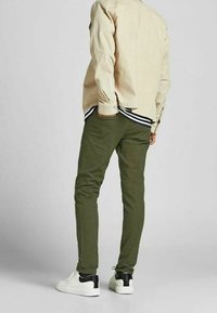 Maglietta beige a maniche lunghe, pantaloni verde oliva e sneakers bianche con dettagli neri, caratterizzate da una vestibilità casual e un design semplice.