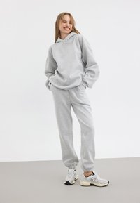 Grå hoodie med oversized passform och framficka, matchad med grå sweatpants. Modellen bär vita och grå sneakers.