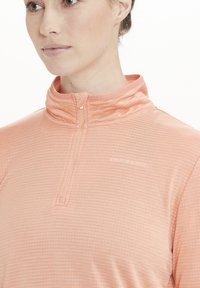 Lettet, struktureret, lyserød atletisk top med lynlåsoplukning og branding på brystet. Stofmet har et diskret rutemønster.