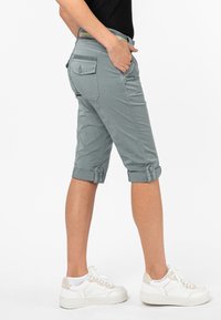 Grijze katoenen bermuda shorts met opgerolde manchetten, zijzakken en een achterzak met een knoopdetail. Gecombineerd met witte sneakers.