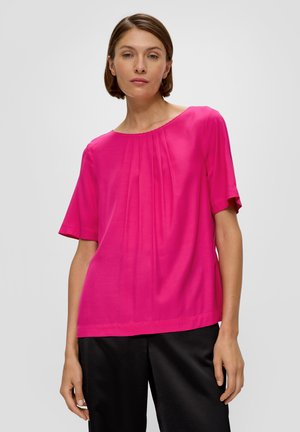 Krótki rękaw t-shirt w intensywnym różowym kolorze, z okrągłym dekoltem i pionowymi fałdami. Gładka struktura z luźnym krojem, w połączeniu z czarnymi spodniami.