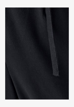 Čierna tkanina s hladkou, matnou textúrou; obsahuje rovný šev a zúženú šnúrku na sťahovanie. Detail zobrazuje šitie a zrno látky.