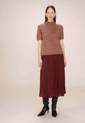 Haut en mohair rose à manches courtes, associé à une jupe plissée bourgogne. Le modèle porte des bottes noires à talons jusqu'aux genoux.