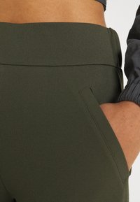 Tmavě zelené kalhoty s vysokým pasem vyrobené z texturovaného materiálu s bočními kapsami a hladkým pasem, které zdůrazňují přiléhavý design.